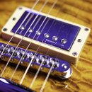 Detail elektrické kytary s viditelným snímačem v krémovém rámečku a chromovaným mostem. Na snímači je nápis Seymour I an. Tělo kytary má žlutohnědou…