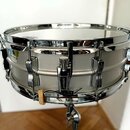 Stříbrný snare drum s chromovaným kováním. Na bočnici je v levé části viditelný neúplný nápis "Ludwig". Nástroj je umístěn na chromovaném stojanu. Po…
