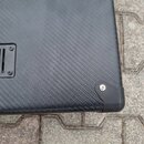 Detailní pohled na roh černého koutu reproduktorového boxu potaženého texturovaným materiálem. V levé části je vidět kovová ventilační mřížka s černý…