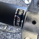 Detailní záběr na černou kovovou trubku s přilepeným obdélníkovým štítkem, na kterém je bílý nápis HAYMAN s registracením znakem ®. Vedle trubky je v…
