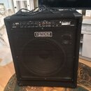Černý basový kombozesilovač s mřížkou před reproduktorem. Na horním ovládacím panelu je nápis RUMBLE 100 a na přední mřížce logo FENDER BASS AMPLIFIC…