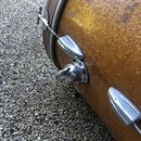 Detailní pohled na část bubnu s hnědým třpytivým povrchem a dřevěným obručem. Na korpusu jsou vidět chromované lugy a kovový mechanismus s knoflíkem.…