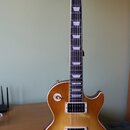 Elektrická kytara s trupem v žlutém gradientu (sunburst) a tmavým hmatníkem s trapezoidními vložkami. Na hlavě je bílý nápis Gibson. Nástroj má dva h…