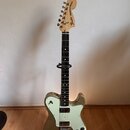 Elektrická kytara s kovově šedým trupem a bílým pickguardem. Na hlavě hmatníku je nápis Fender TELECASTER DELUXE. Nástroj má černý hmatník, dva humbu…