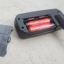 Černý plastový adaptér na baterie s kovovým 6,3mm jack konektorem. Uvnitř jsou umístěny dvě červené AAA baterie s nápisy „SUPER HEAVY DUTY“ a „AAA R0…