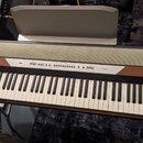 Digitální piano s klávesnicí, kombinací dřevěného a šedého povrchu. Na ovládacím panelu je vlevo nápis KORG a vpravo označení modelu SP-250. Nad kláv…