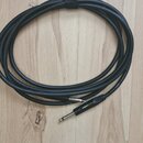 Černý audio kabel s konektory typu jack, svinutý do kruhu a zajištěný černým suchým zapínáním. Na jednom z konektorů je viditelný bílý nápis "BELDEN"…
