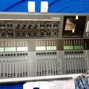 Šedý digitální mixovací pult s černými ovládacími prvky a displejem v pravé horní části. V levém horním rohu je nápis iLive-T112 a uprostřed nahoře z…