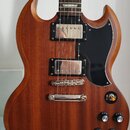 Elektrická kytara s hnědým dřevěným korpusem, černým pickguardem a dvěma humbuckery. Na hmatníku jsou vidět bílé trapézové vložky. Nástroj je umístěn…