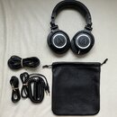 Černá uzavřená sluchátka s logem Audio-Technica na mušlích a nápisem ATH-M50x. Součástí je černý textilní vak s vyraženým nápisem Audio-Technica Corp…