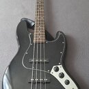 Černá elektrická basová kytara s černým pickguardem a hnedým hmatníkem. Na hlavě nástroje je viditelné logo Squier. Instrument má dva snímače a tři o…