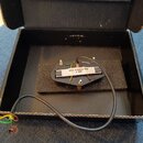 Černý elektrický snímač s bílým plastovým krytem, umístěný v černé krabičce na pěnové podložce. Na krytu je černý nápis MR-T RM PICKUPS 4/26. Snímač…