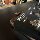 Černý efektový pedál s nápisy M9 STOMPBOX MODELER a DELAY | MOD | DISTORTION | REVERB | ECHO. Na ovládacím panelu jsou viditelné označení FX 0 UNIT,…
