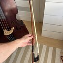 Na fotografii je hnědý smyček z dřeva s bílým vlasem, který drží ruka. Smyček nemá žádné viditelné značky ani loga. V pozadí je vidět část tmavě hněd…