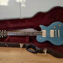 Modře lakovaná elektrická kytara typu Les Paul v černém tvrdém kufru s červeným polstrováním. Na hlavě hmatníku je bílý nápis Summit a text MADE IN K…