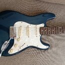 Tmavě modrá elektrická kytara typu Stratocaster s bílým perleťovým pickguardem a hnedým hmatníkem. Na kytare jsou tři snímače typu single-coil, jeden…