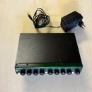 Černý rackový efekt s zeleným předním panelem a přiloženým napájecím adaptérem. Na panelu je nápis JOEMLEK a sekce s popisky OPTICAL COMPRESSOR a MEE…