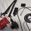 Sada vybavení pro nahrávání složená z červeného audio rozhraní s nápisem Focusrite, černého mikrofonu a černého mikrofonního ramene. Na rameni je vid…