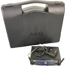 Černý plastový kufřík s vyraženým logem AKG. Před ním je umístěn bezdrátový přijímač s nápisy SR 40 a AKG Wireless System, vysílač s logem AKG a kabe…