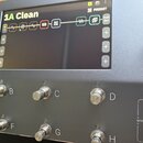 Detailní pohled na digitální procesor efektů s displejem a ovládacími prvky. Na displeji je nápis 1A Clean, ikony efektů a tlačítko PRESET. Pod displ…