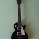 Černá elektrická kytara s tvarem single-cut a bílým pickguardem. Na hlavě hmatníku je bílé logo Epiphone. Nástroj má dva humbuckery s krémovými rámeč…