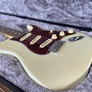 Krémová elektrická kytara typu Stratocaster s hnědým želvovinovým pickguardem a třemi snímači. Nástroj je umístěn v otevřeném černém kufru s šedým pl…