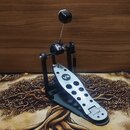 Fotografie zobrazuje jednoduchý pedál basového bubnu v černé a stříbrné barvě. Na stříbrném šlapadle je viditelný nápis V4 a v dolní části označení B…
