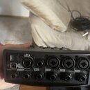 Záběr na zadní panel černého audio rozhraní nebo mixeru. Jsou zde viditelné vstupy a výstupy s popisky: Master, Outputs, Aux, 4/5, Line IN, 3, Preamp…