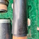 Detailní pohled na části dřevěných dechových nástrojů v zeleném pouzdře. Na černém povrchu jednoho z nástrojů je vyrazen nápis P46381. Vedle něj je v…