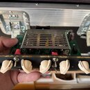Fotografie zachycuje přední panel elektronického zařízení s ovládacími prvky, umístěný na zelené základní desce s kovovým chladičem. Na panelu jsou č…