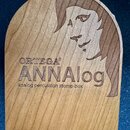 Dřevěný perkusní přístroj s oblým horním okrajem. Na povrchu je vyryto logo ORTEGA®, název ANNAnalog a nápis analog percussion stomp box. Vedle textu…