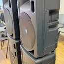 Čtyři černé plastové aktivní reproduktory v plastových krytech, naskládané na sebe ve dvou sloupcích. Na přední mřížce každého reproduktoru je v cent…