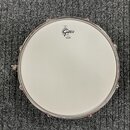 Fotografie znázorňuje snare drum z pohledu shora. Bílá membrána nese černé logo „Gretsch“ a pod ním menší nápis „made by REMO“. Obruč je kovová, chro…