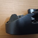 Detailní pohled na černý plastový držák nebo příslušenství s texturovaným povrchem. V horní části je vidět kousek tmavé pěny nebo gumového tlumiče. N…