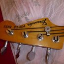 Fotografie zachycuje hlavu basové kytary z přírodního dřeva s lakovaným povrchem. Na hlavě jsou nápisy „Fernandes“ a „POWER BASS“. Jsou zde vidět čty…