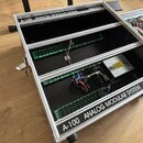 Otevřený hliníkový kufřík s černým vnitřním povrchem, který obsahuje elektronické komponenty na zelených plošných spisech a chladič s napájecím zdroj…