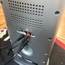 Zadní strana stříbrného elektronického zařízení s ventilačními otvory. V sekci INPUT STEREO jsou do červeného a bílého RCA konektoru zapojeny dva kab…
