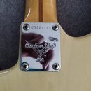 Detail krku a spoje s tělem elektrické kytary z jasného dřeva. Na kovém krytu spoje je vyryto logo Custom Shop USA a v horní části je vyraženo sériov…