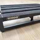 Černý kovový pedalboard s povrchem z černého plstěného materiálu. Na boku je viditelné logo s nápisem ROCKBOARD® by WARWICK. Povrch a hrany nástavce…