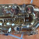 Detailní pohled na část saxofonu s lakovaným zlatým povrchem. Jsou vidět klapy, mechanismus a spojovací šrouby. Na nástroji nejsou žádné čitelné znač…