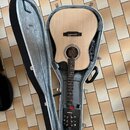 Akustická kytara s přírodním povrchem korpusu a tmavým hmatníkem v otevřeném tvrdém kufru. Na hlavě nástroje je viditelné logo "Ibanez". Povrch nástr…