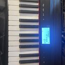 Detailní pohled na klávesnici digitálního piana s černým šasi. Na podsvíceném displeji je zobrazen text [PIANO1], GO Grand a číslo 01. Nad displejem…