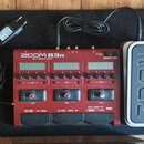 Červený multi-efektový procesor s nápisem ZOOM B3n Multi-Effects Processor. Zařízení má tři displeje, ovládací knoflíky a tři nožní spínače označené…