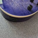 Detailní pohled na spodní hranu modré elektrokytary s výraznou masou dřeva. Na hraně je umístěn černý vstupní jack. Povrch nástroje je lakovaný s vid…