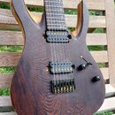 Elektrická kytara s tmavě hnědým dřevěným korpusem a výraznou strukturou zrna. Nástroj má dva černý humbuckery se zlatými pólky a černý most s gold h…