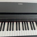 Černý digitální klavír s bílými a černými klávesami. Na horním krytu je bílé logo a nápis YAMAHA. Povrch nástroje vykazuje drobné prachové nečistoty.