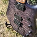 Detail elektrické kytary s fialovým lakovaným povrchem s výraznou strukturou dřeva. Nástroj má dva černá humbuckery, černý most a tři černé oválné kn…