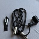 Černý kabel s dvěma stříbrnými konektory typu XLR. Vedle kabelu je černý plastový držák a černá textilní šňůrka s bílým nápisem SHURE. Všechny kompon…
