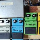 Fotografie zobrazuje několik efektových pedálů značky BOSS. Jsou zde modely Noise Gate NF-1 v bílé barvě, Chorus CE-2 v modré barvě a Phaser PH-1 v z…