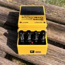 Žlutý efekt pedál s černými ovládacími knoflíky a černým spínacím pedálem. Na horní části je nápis Bass OverDrive ODB-3 a logo BOSS. Jsou zde označen…